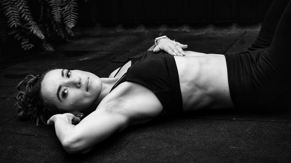 A woman in a sports bra lying on the floor in a contemplative pose.
